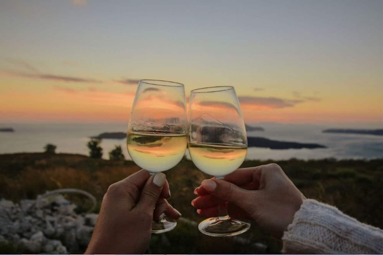Two glasses of Santorini white wine raised at sunset above the caldera